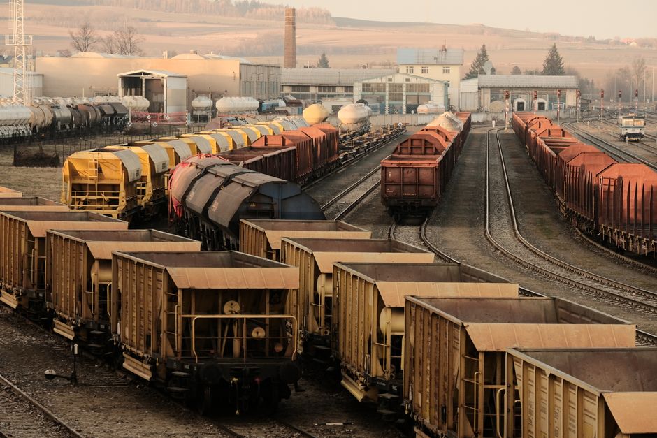 Infraestrutura Logística — A busy freight train yard with multiple tracks and a variety of train cars in a rural setting.
