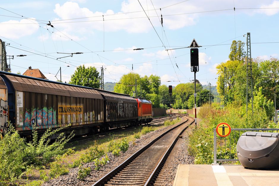 Infraestrutura Logística — Freight train passes through a lush, green railway track on a sunny day.